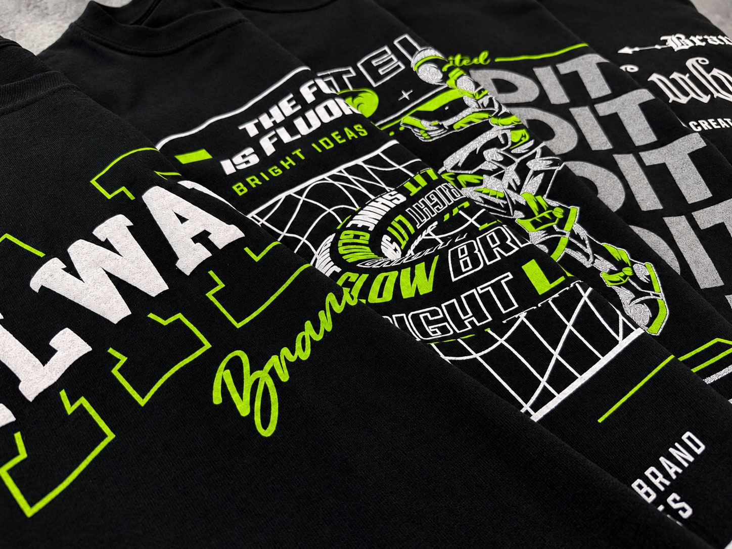 Close-up of layered black apparel with lime-green and white screen-printed brand graphics